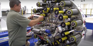 Illustration for article titled This Robot Is a Loom For Weaving Carbon Fiber Into Rocket Parts